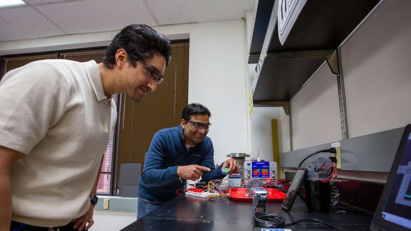 Two people work in a lab over a computer while testing a thermomagnetic generator.