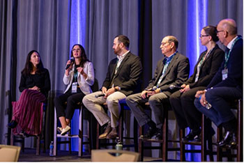 A group of people hold microphones and sit in tall chairs on a stage.