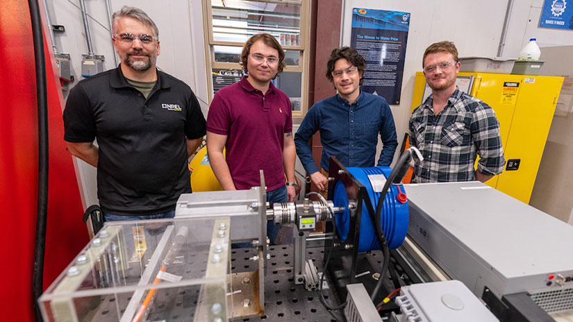 Four people standing behind a collection of hardware and wires