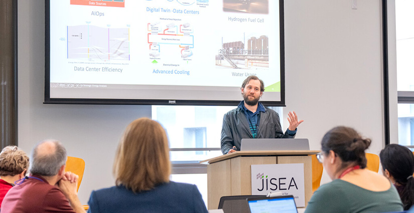 A person presenting behind a podium with a small audience watching.