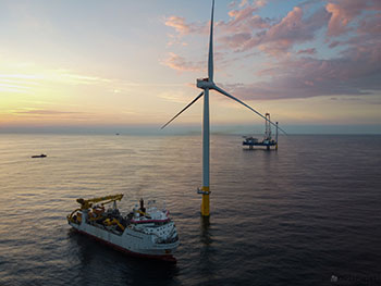 Photo of an offshore wind turbine with a servicing ship next to it in the ocean