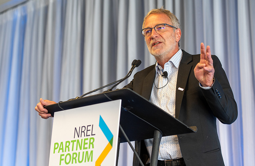 A man holds up three fingers while speaking at a podium.
