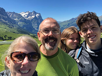 Four people stand in front of snow capped mountains