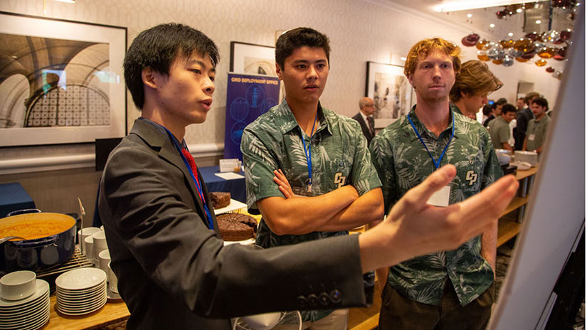 Three students look at and discuss research poster