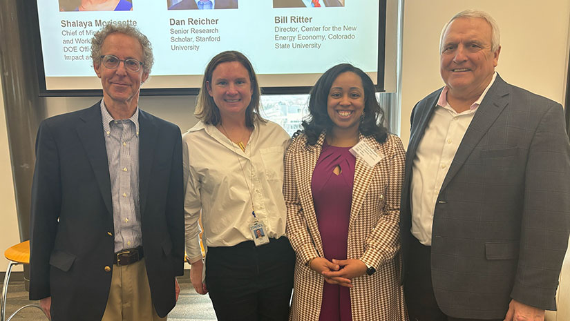 Four people stand together in front of presentation screen