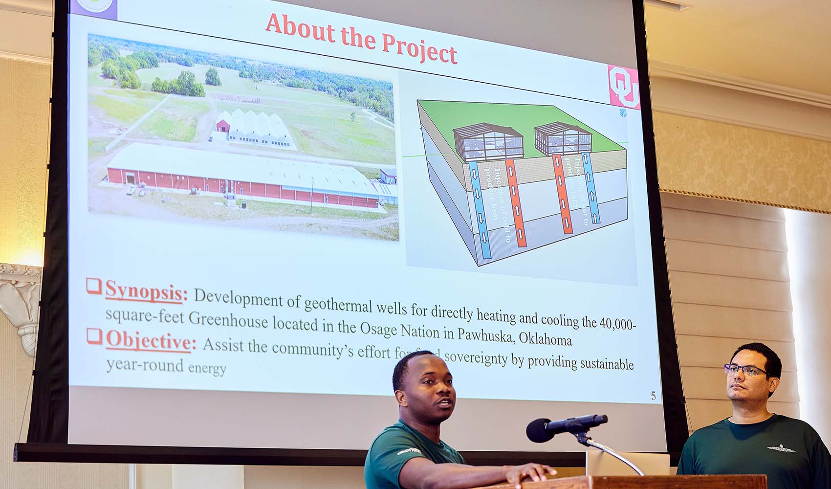 A student presents at a podium with a presentation slide behind him titled About the Project.