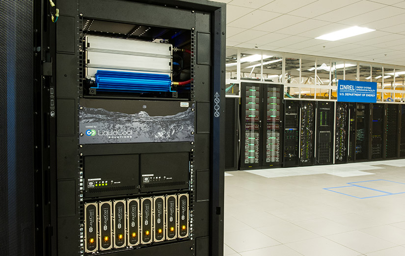 A server rack sits in a server room with more servers in the background. 