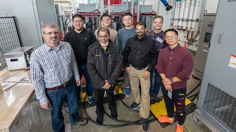 A group of eight people posing in a lab with electrical cable