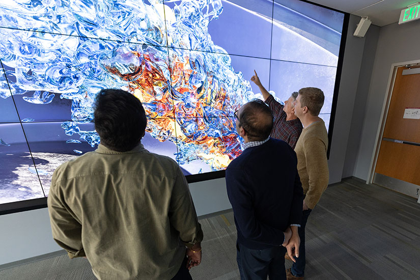 Four people in a room facing a large screen of 3D images.