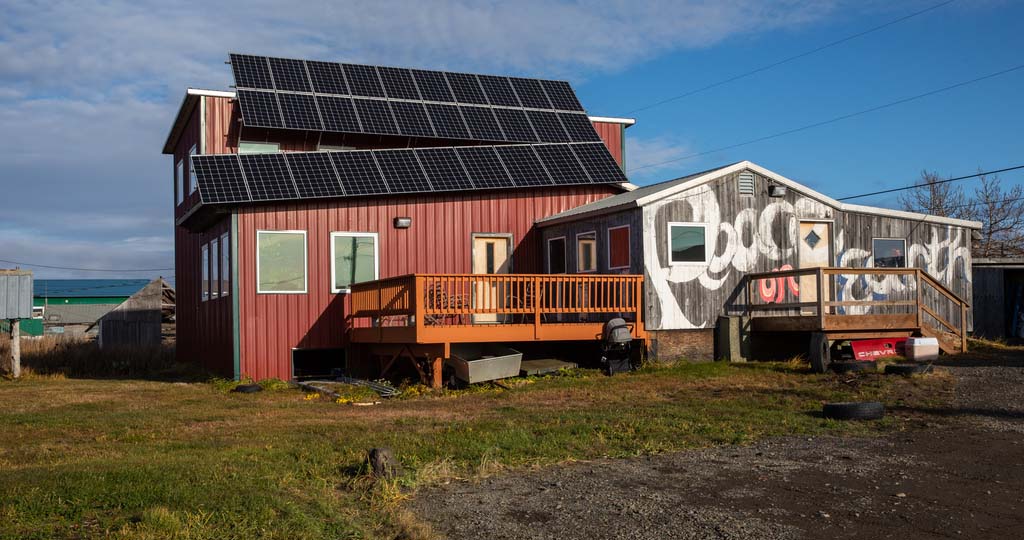 A wooden building with solar panels and the words 'Peace On Earth' painted on the side.