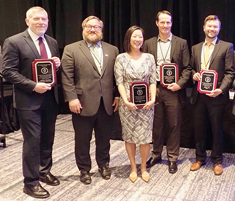 A group of people smiling while holding awards.