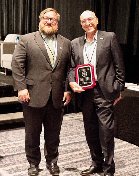 Two smiling for a picture while one of them holds an award.