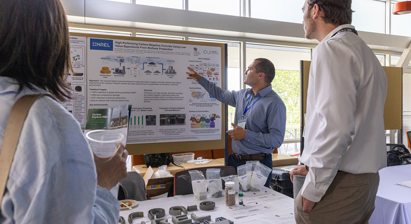 A person presents a poster on concrete to two other people.