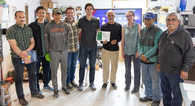 Nine people pose with a certificate in a community room.