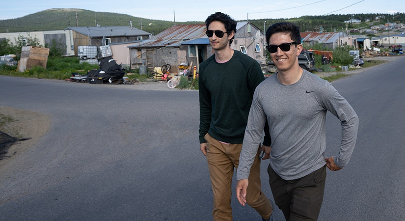 Two individuals walk through a small town.