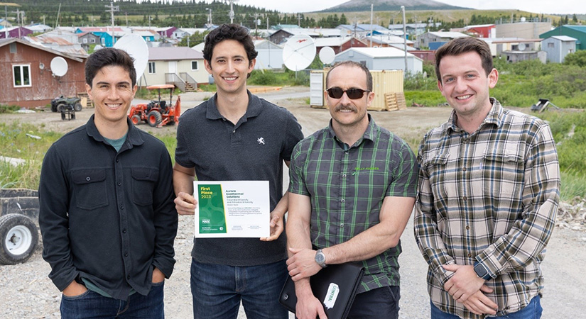 Four individuals pose holding a certificate in front of a small town.