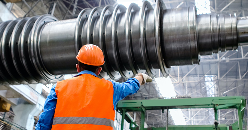 A man in a hard hat and safety vest pointing at a large metal component.