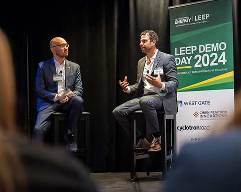 Two men sitting on a stage while speaking to an audience.