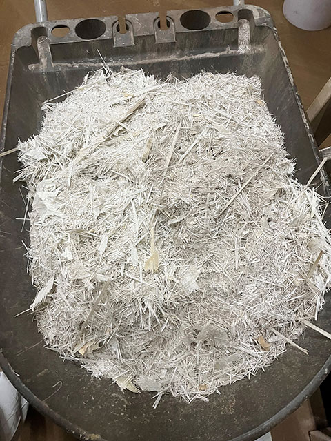 A wheelbarrow filled with wind turbine blade cuttings that are long, thin, and white.