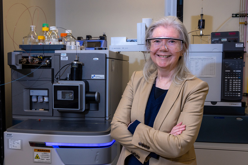 A person wearing safety goggles poses with their arms crossed in a lab.