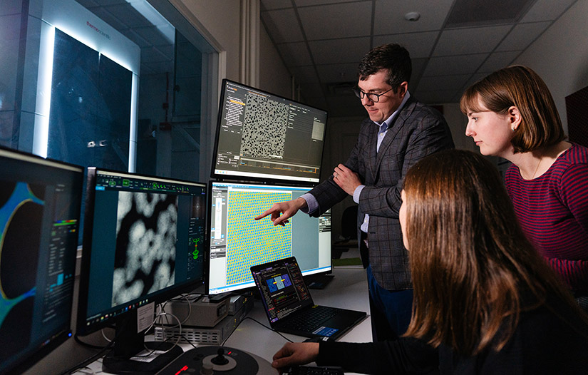 Three researchers look at a screen in a lab.