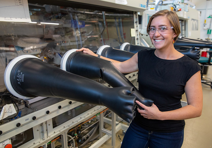 A person wearing safety goggles stands next to an anaerobic chamber.
