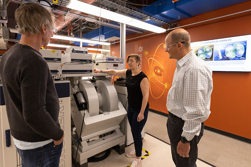Three people stand next to equipment in a lab.