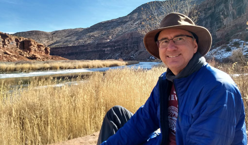 Continue reading about A man sits on a river bank with cliffs in the background.