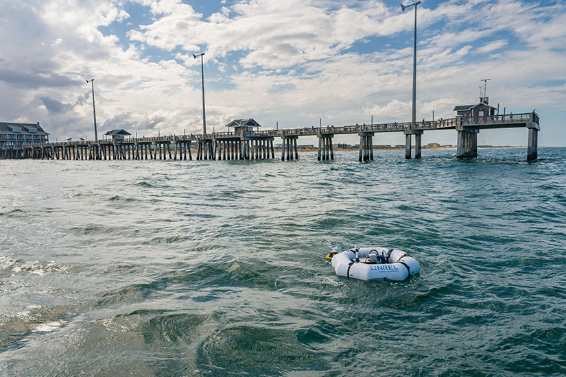 A device floating in the ocean in front of a pier.