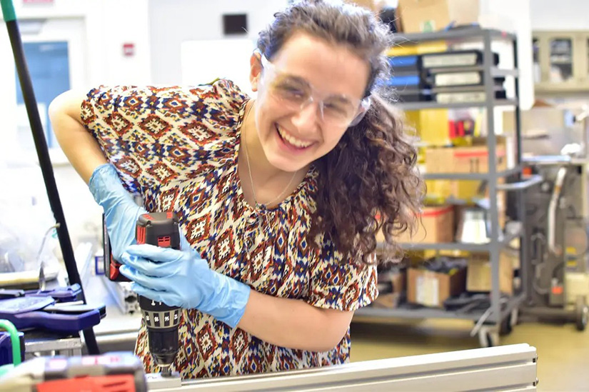 A person wearing safety goggles and gloves uses a power tool in a lab.