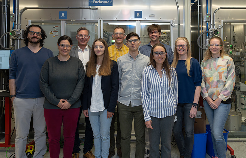 Ten people stand in front of laboratory equipment.