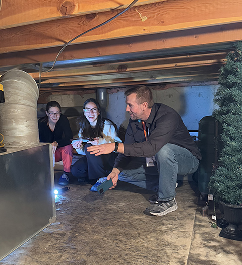 Three people kneel in a crawlspace.