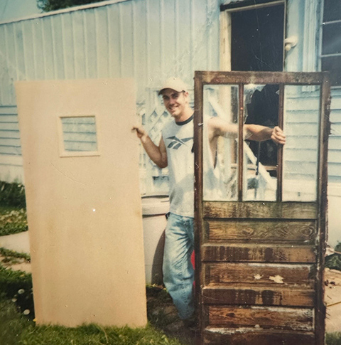 A person standing in between a new door and an old door.
