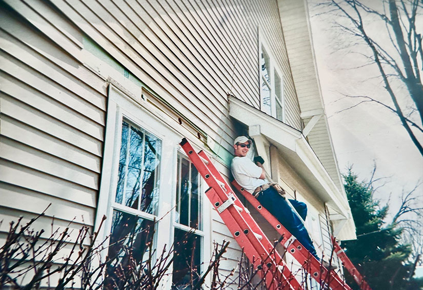 A person stands on a ladder leaning against a house.