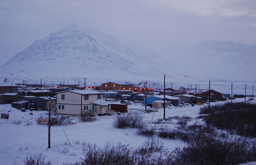 Village of Anaktuvuk Pass, Alaska, in winter, with snow-covered ground, houses, and mountains in the background.