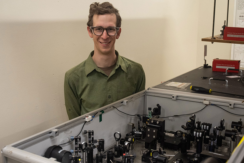 A researcher poses behind a table in a lab.