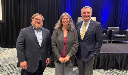 Continue reading about Three people pose in front of a stage.