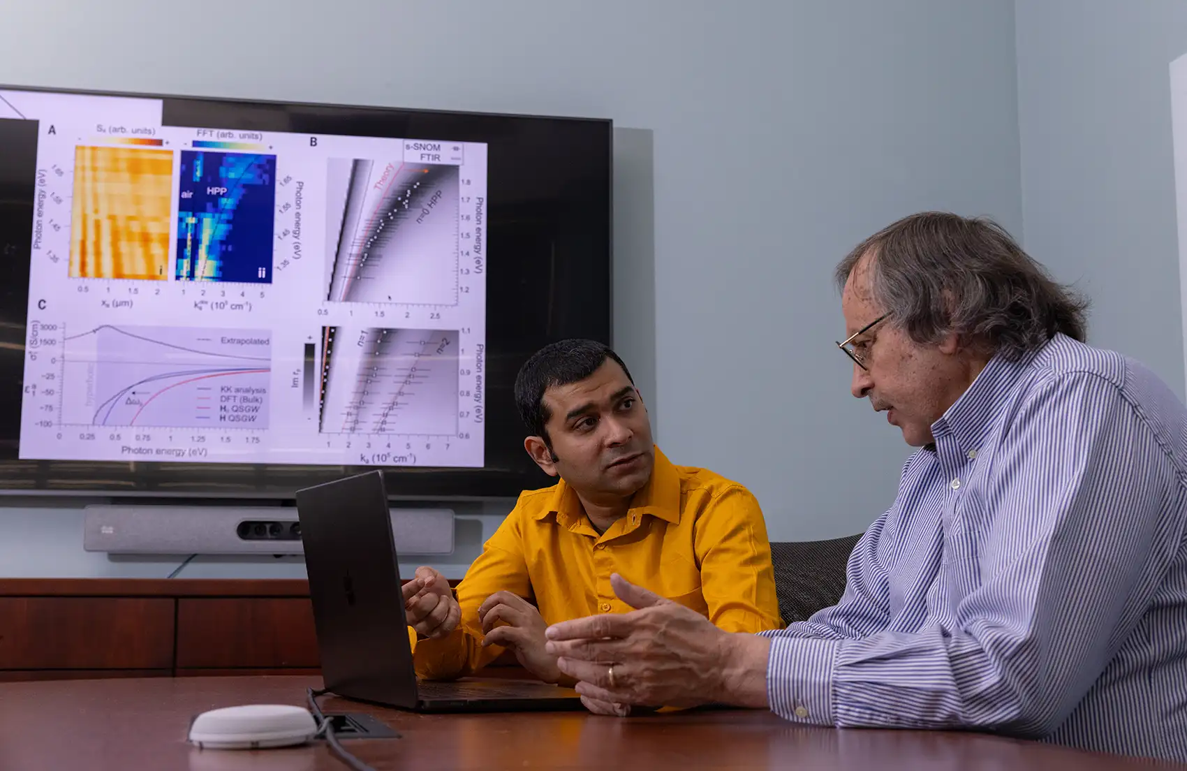 Two NREL researchers  discuss their research next to a laptop with data on a monitor screen.