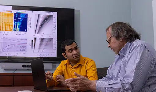 Continue reading about Two NREL researchers  discuss their research next to a laptop with data on a monitor screen.