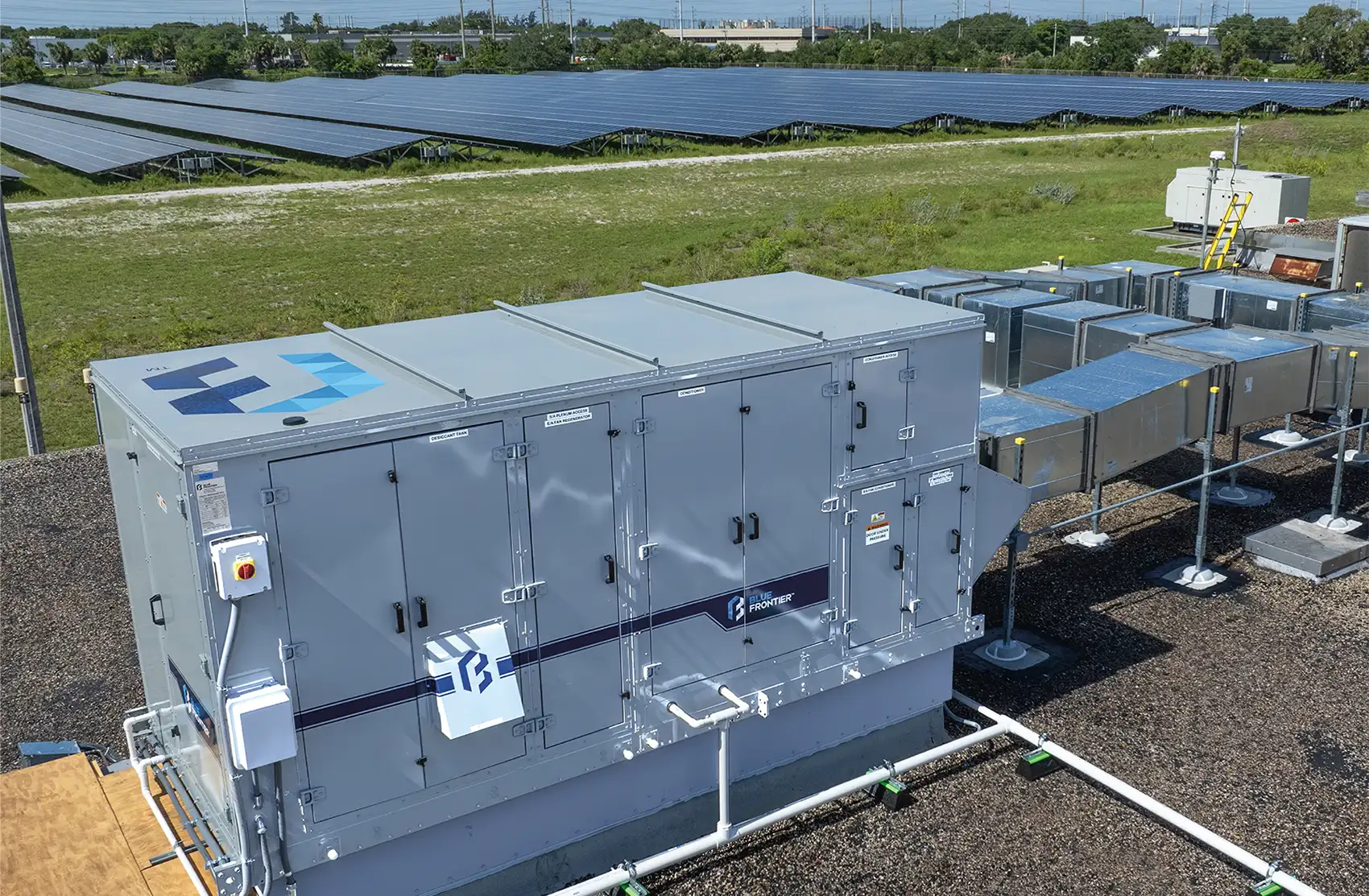 Photo of a large metal air conditioning unit with vents and access panels. The unit is adjacent to a field of photovoltaic panels.