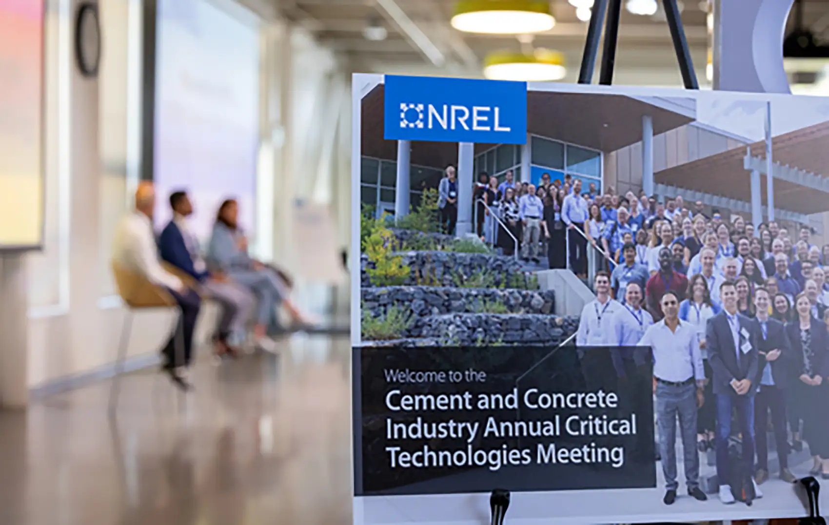 Close up of a sign that says “Welcome to the Cement and Concrete Industry Annual Critical Technologies Meeting” with a panel of three individuals in the background.