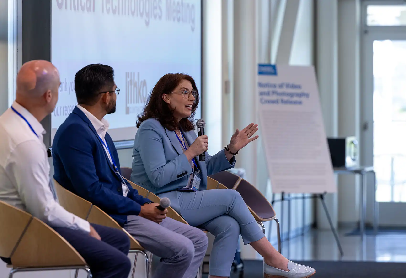 Three people sit in front of a screen, one holding a microphone.