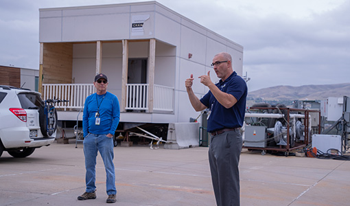 Continue reading about Shanti Pless speaks to a group of people in front of a modular apartment prototype.