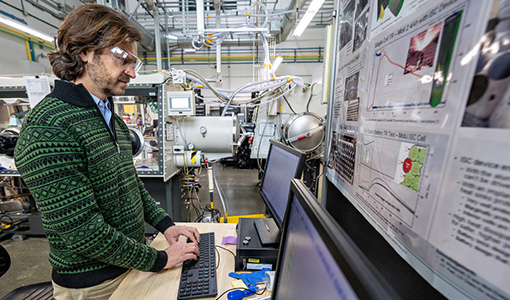 Continue reading about A person wearing safety goggles works on a computer in a lab.
