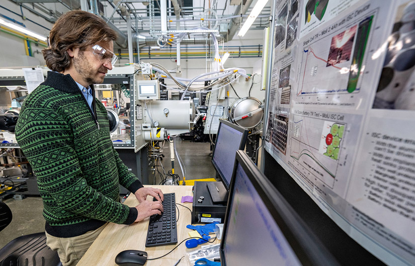 A person wearing safety goggles works on a computer in a lab.