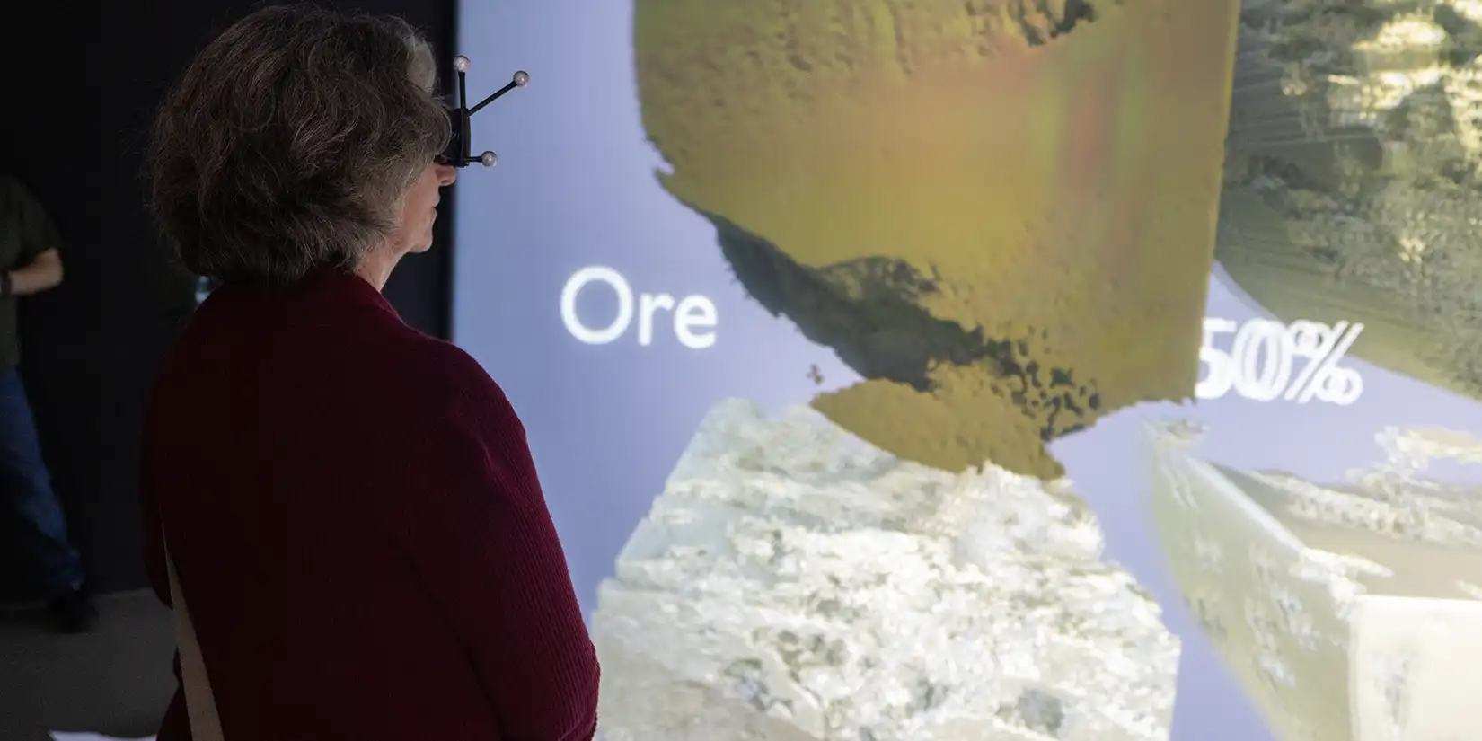 104795-full Woman wearing 3D glasses views a large data visualization screen showing mineral ore imagery and processing statistics