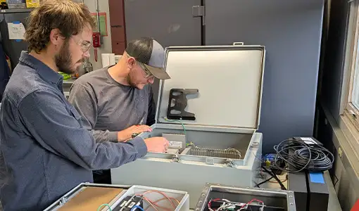 Continue reading about Two people look inside a box containing machinery.