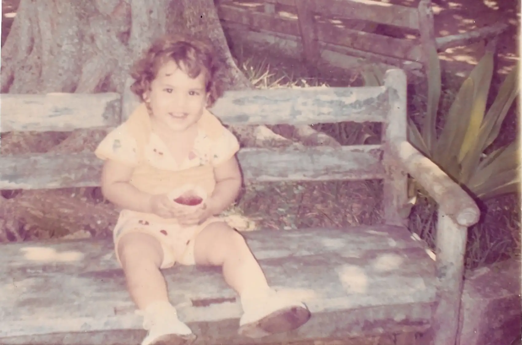 A child smiling and sitting on a bench holding a cup with shaved ice.