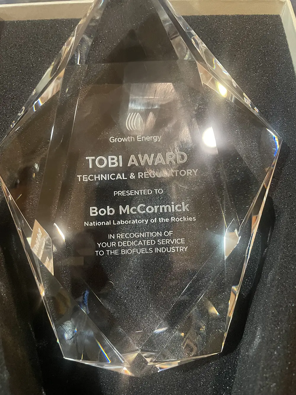 20260325-accomplished-researcher-recognized-by-major-industry-association-for-leadership-in-biofuels-research-robert-mccormick-tobi A transparent glass award plaque.