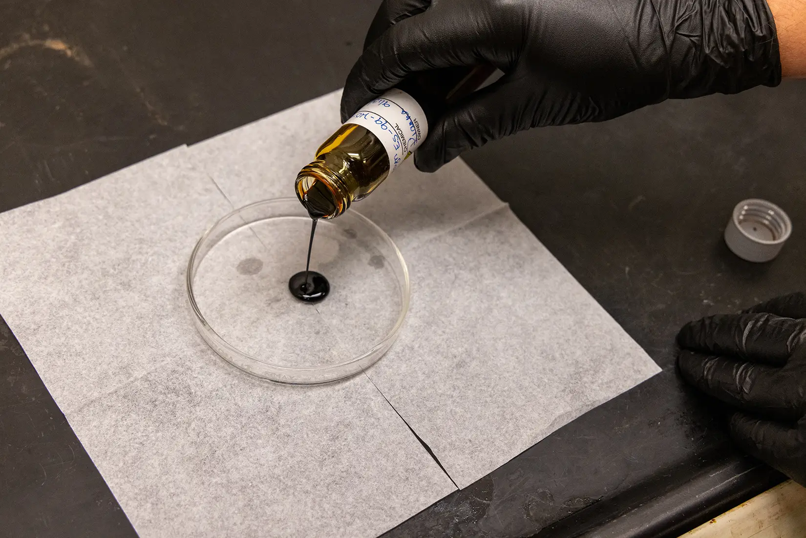 A researcher pours black pyrolysis oil into a petri dish.